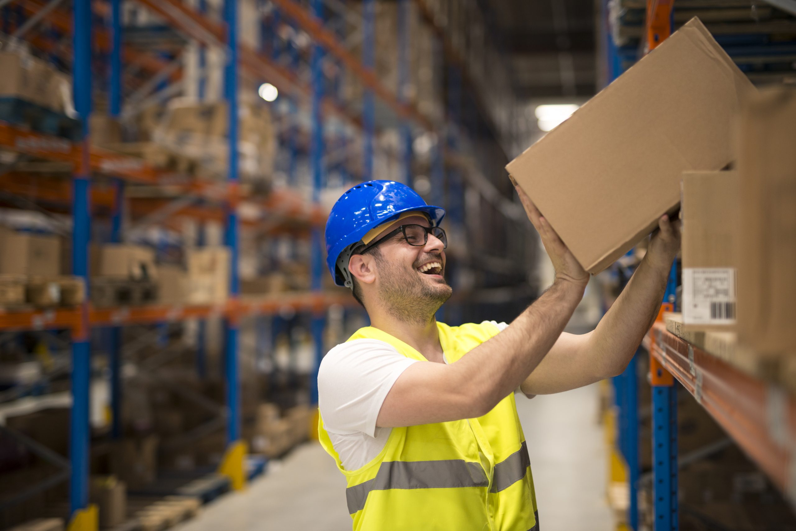 Smiling warehouse worker moving boxes on the shelf.